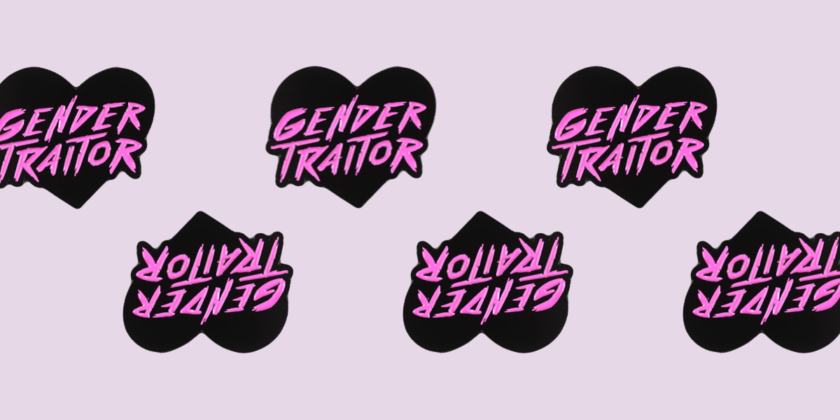 A black and pink heart shaped enamel pin. The words GENDER TRAITOR are in a textured painted typeface.