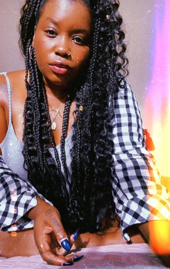 Image shows black woman in bed with long braids wearing a gray. black and white loungewear outfit.