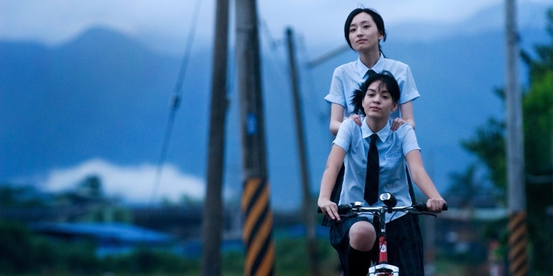 Two girls in school uniforms ride on a bike together.
