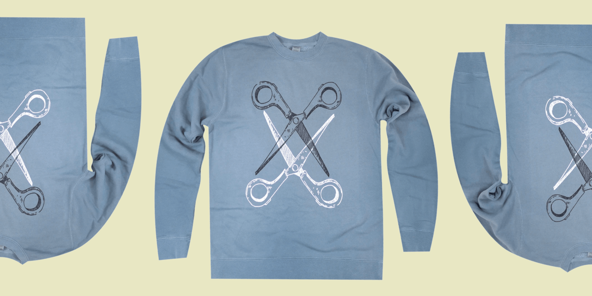 Scissoring sweatshirt is a classic cut in a medium blue tone. Two pairs of scissors — one black and one white — intersect.