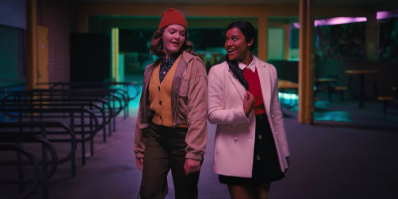 Two girls dance outside at a high school in neon lights.