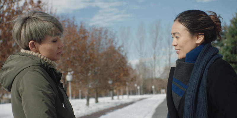 Two women talk with a snowy backdrop behind them.