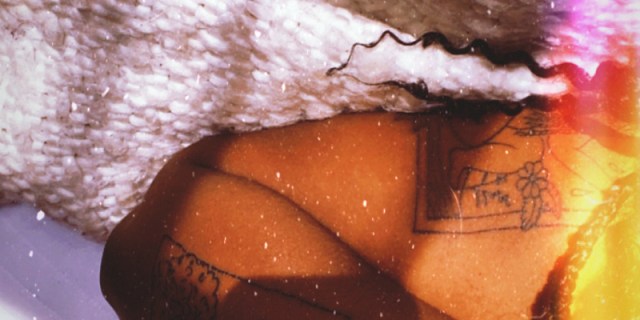 Image shows black woman in bed with tattoos on her arm with 3 different textured blankets surrounding her.