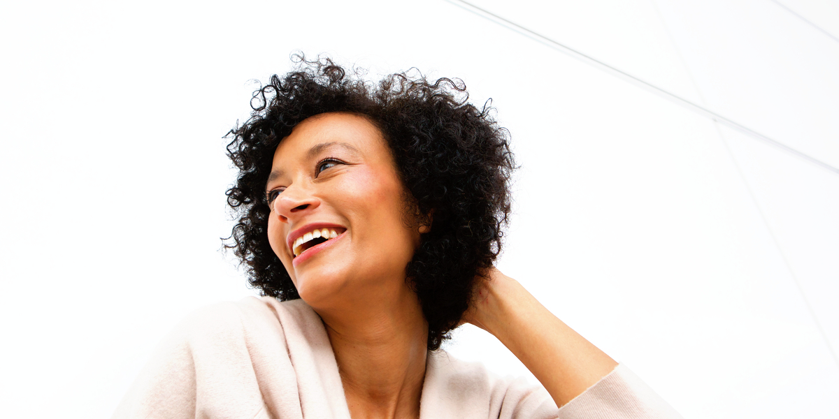 An older woman with short curly hair looks to the side, laughing at something out of frame