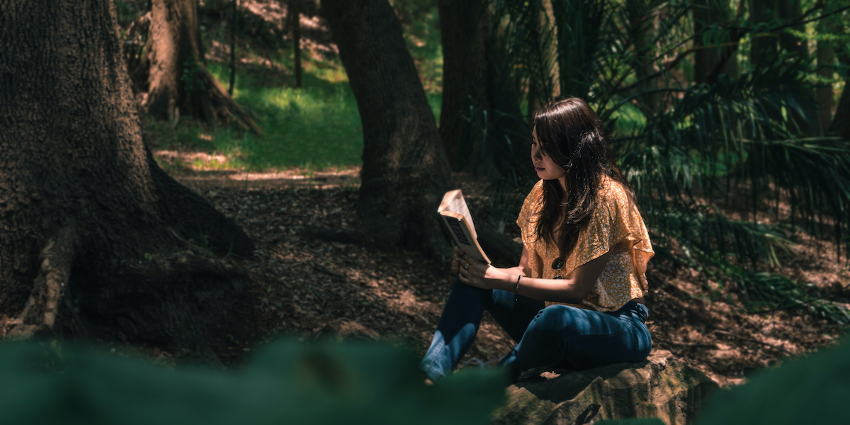 someone with long hair reading in a forest