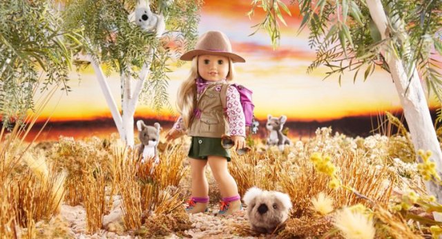 A blonde American Girl doll is posed as if she is hiking with Koalas in Australia. She has on a pink backpack.