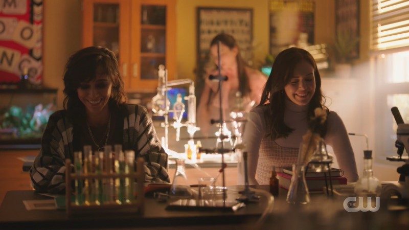 Scene from Legacies: Finch and Josie laugh and smile while sitting at a high school science lab table together.