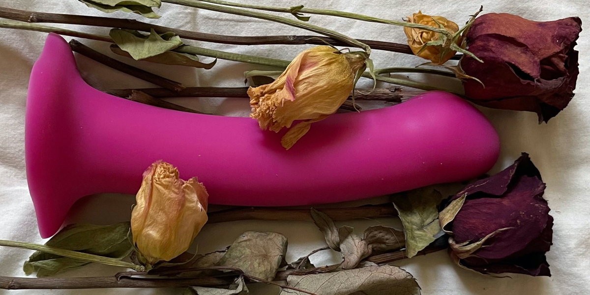 a purple dildo lies in a bouquet of dead roses