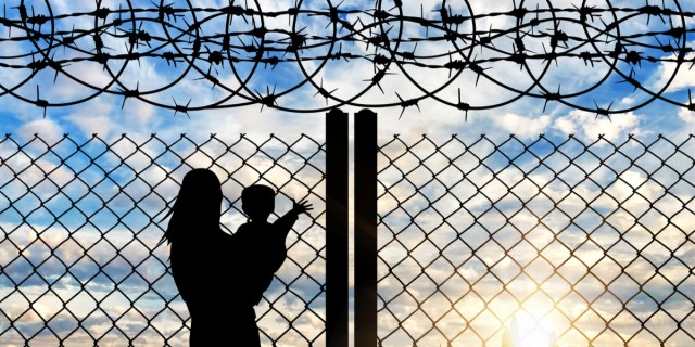 A shadow of a mother and child against a sunset on a barb wire fence