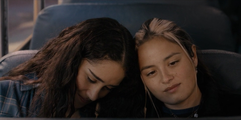 Greta and Riley lean their heads together listening to music on the bus