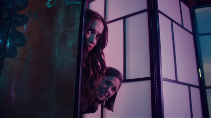 Waverly and Wynonna poke their heads out from behind a wall to spy on Amon.