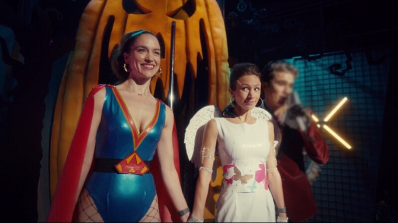 Wynonna, dressed as a sexy superhero, and Waverly, dressed as an angel, walk out onto the Glory Hole stage holding hands.