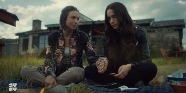 Scene from Wynonna Earp: Waverly holds her sister's hand as she looks at her with love, Wynonna smiles softly and a bit sadly down at their clasped hands.