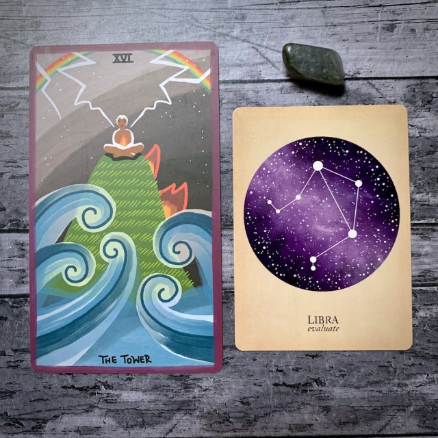 A photo of the tarot card for The Tower and the astrological card representing Libra, along with a small crystal