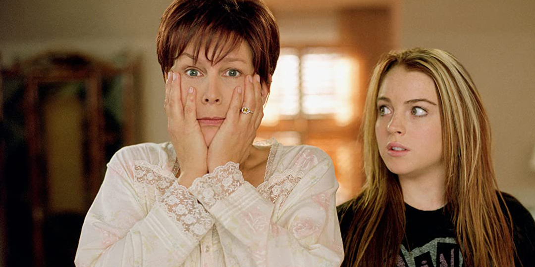 In a screenshot from Freaky Friday, Jamie Lee Curtis has her hands covering her face in a worried stare into the camera, and a teenage Lindsey Lohan looks at her with a despairing side-eye