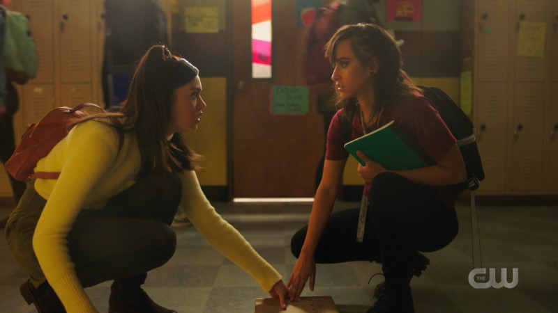 Josie and Finch both lean down for the same book and make eye contact as their fingers brush.