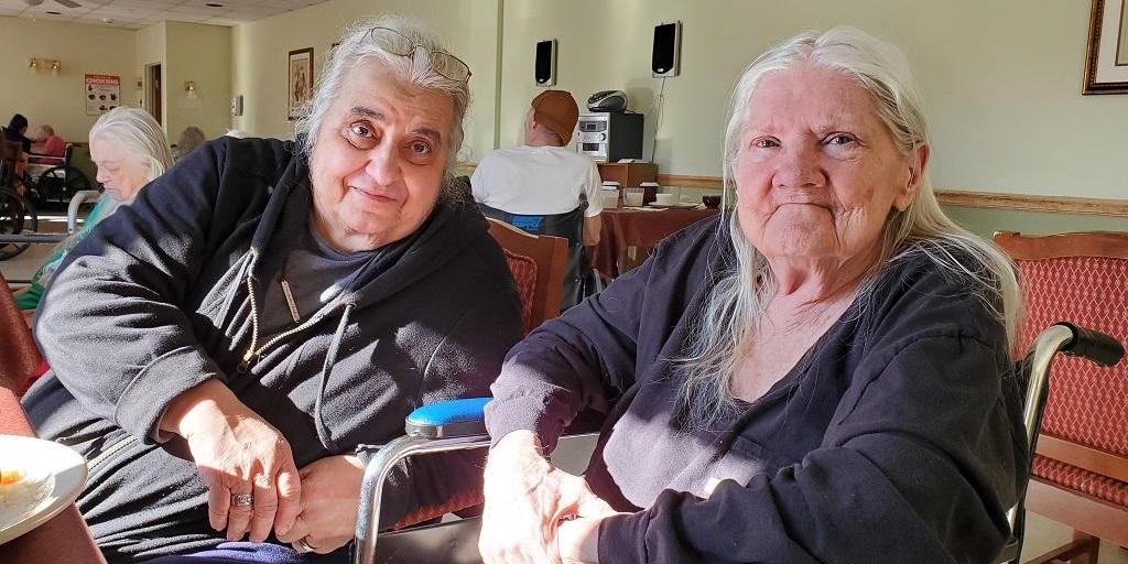 Two older women, Marie Giardino and Michaeljon Blue, sit next to each other at the Hornell Gardens nursing home. Blue is in a wheelchair.