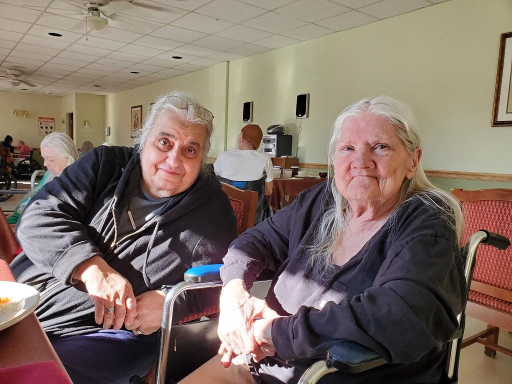 Two older women, Marie Giardino and Michaeljon Blue, sit next to each other at the Hornell Gardens nursing home. Blue is in a wheelchair.