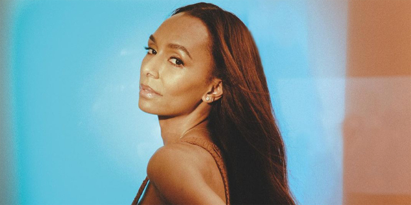 Janet Mock is against a blue background, lit in warm red tones