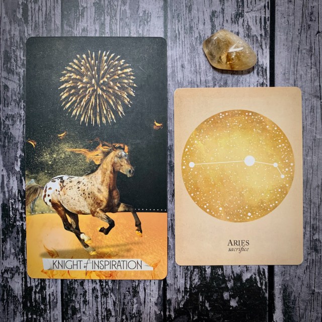 A photo of the card Knight of Inspiration, which features a galloping horse, a constellation card that reads Aries: Sacrifice, and a yellow crystal