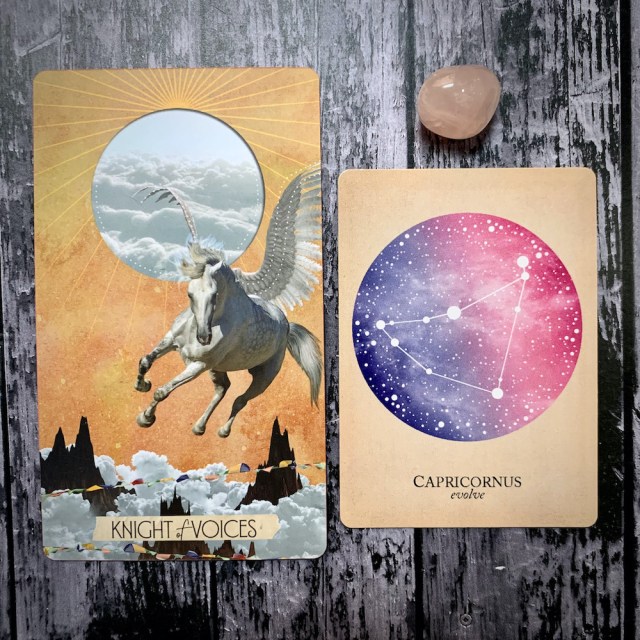 A tarot card for the Knight of Voices featuring a white pegasus flying through a golden sky, a constellation card reading Capricornus: Evolve, and a translucent pink crystal.