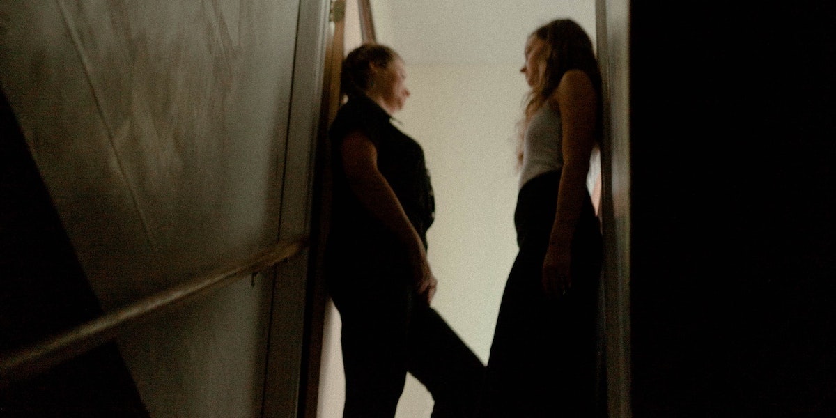 Two women standing inside a doorframe in a dark space, turning to look at each other