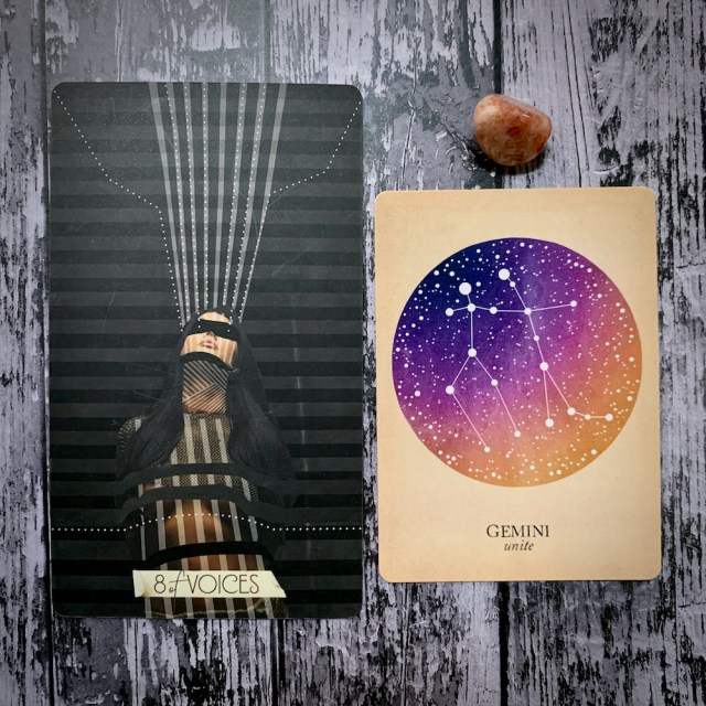 A tarot card for the 8 of Voices, which features a woman in harsh shadow, a constellation card that reads Gemini: Unite; and a variegated pink crystal