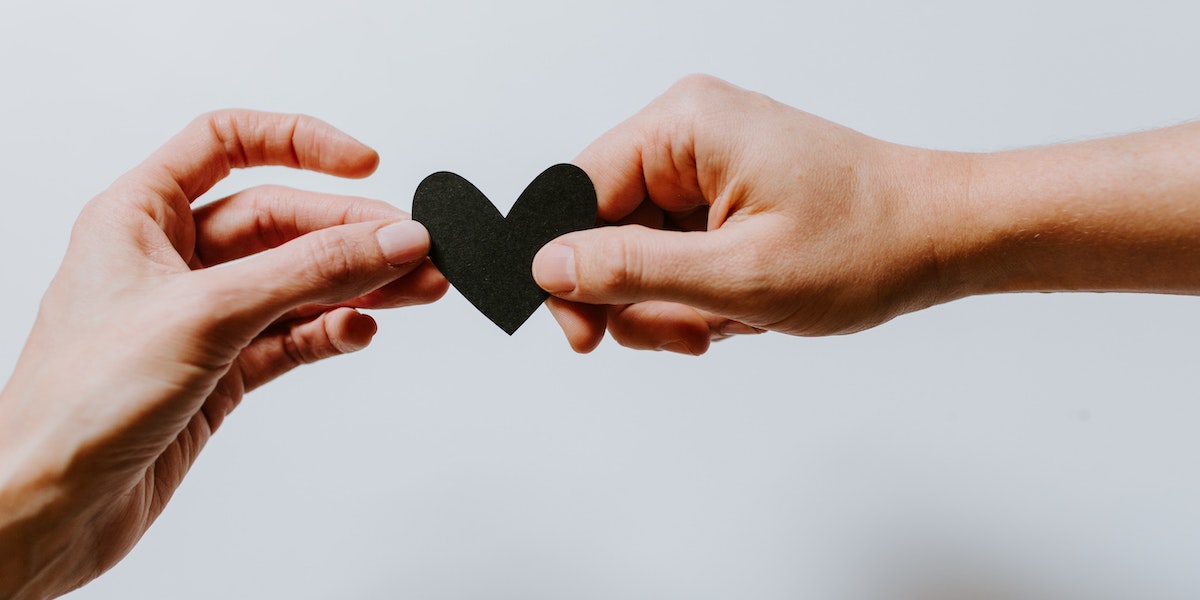 A stylized photo of two hands holding between them a black paper heart.