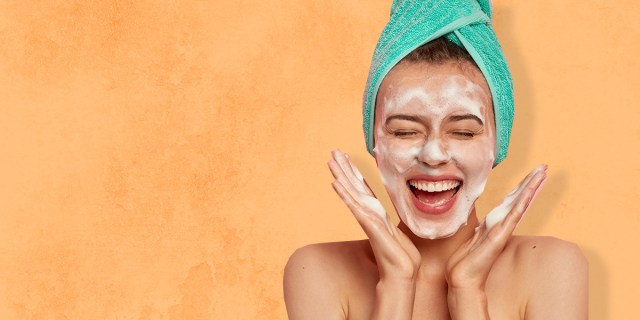 A woman smiles while washing her face