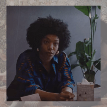 Image shows photo of a Black woman at a desk with her hands clasped together.