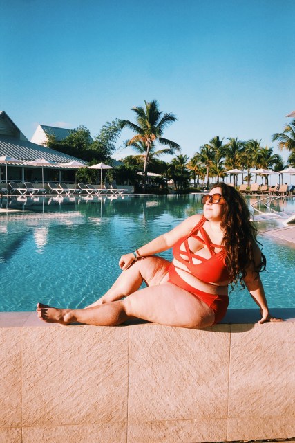 Vanessa lounges by the pool in a two-piece red-orange swimsuit with a scrappy bikini top