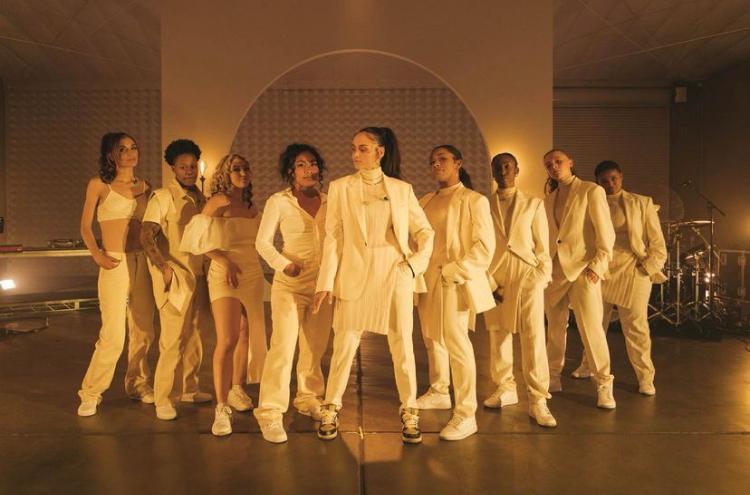 Image Shows Kehlani in her all white suit surrounded by their band who are also all wearing white.