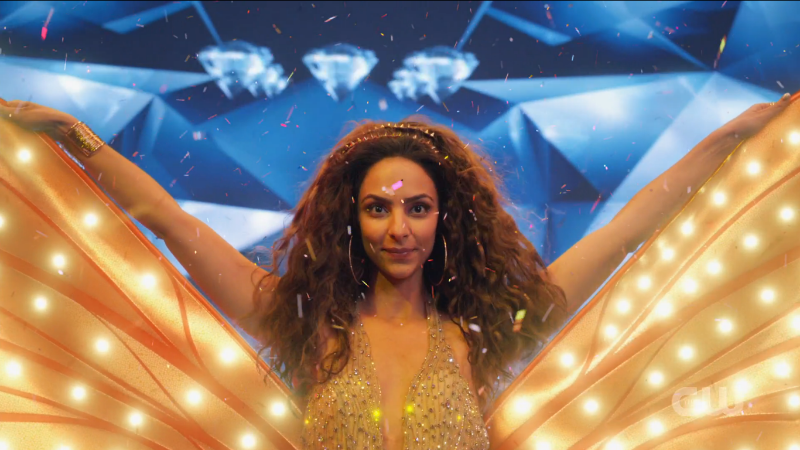 Legends of Tomorrow 603 Zari is surrounded by glitter and extending costume wings at the end of a singing performance.