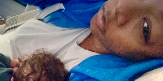A close up of Samira Wiley looking very tired in a blue hoodie with her newborn daughter, George, in her arms.