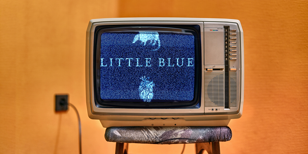 A vintage television set sitting on top of a stool in a warm-toned room with the text LITTLE BLUE showing on a static-y screen