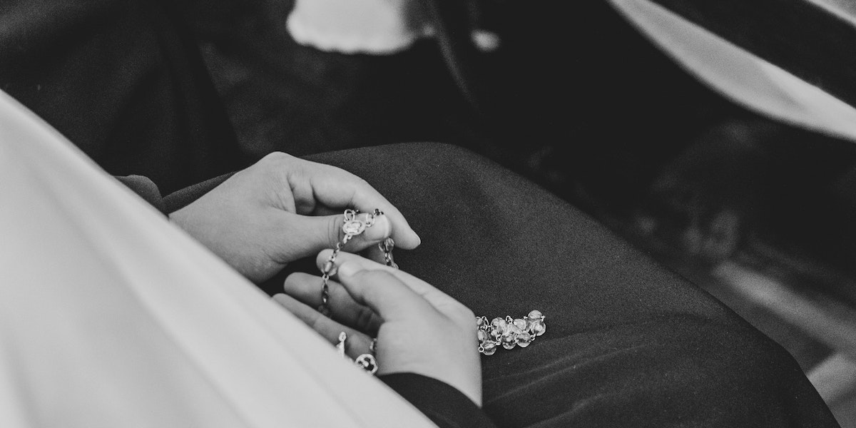 A black and white photo of a pair of hands holding a rosary in a lap.