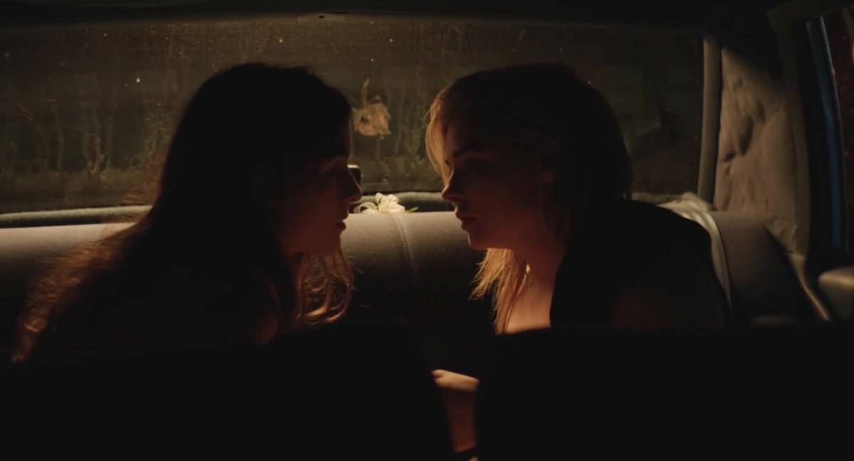 Two girls in the back of a car look at each other intensely