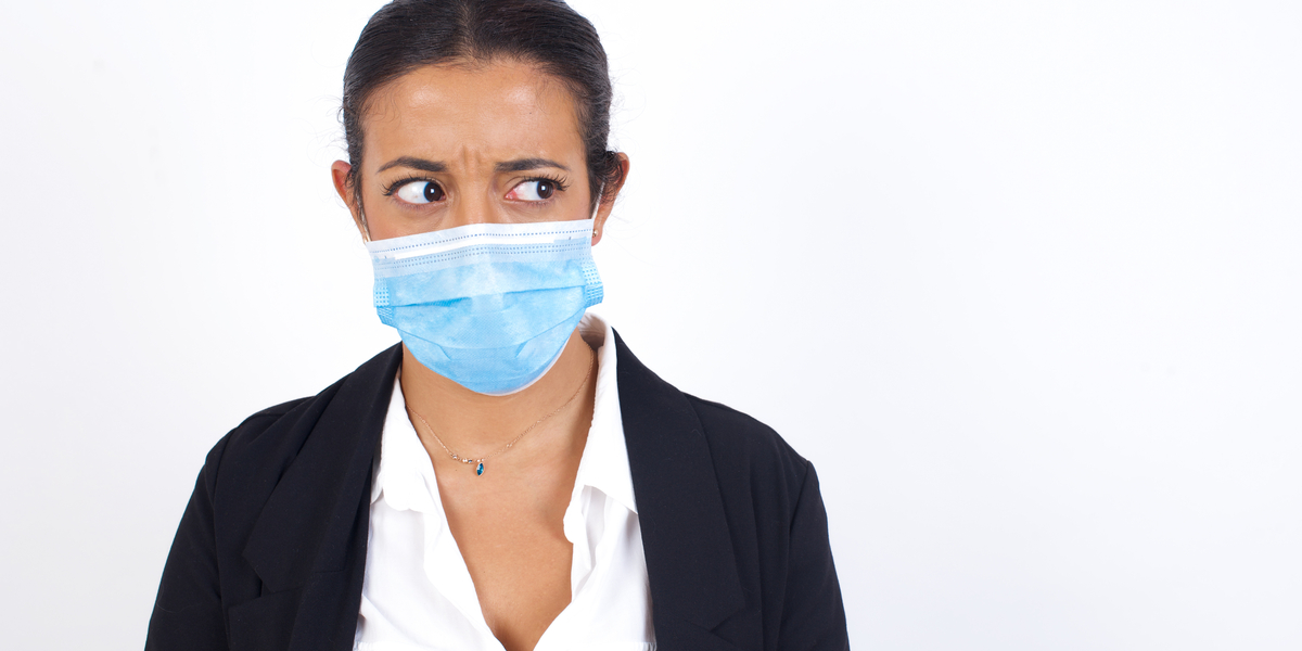 A woman in professional dress looks unsettled while wearing a disposable paper mask over her nose and mouth.