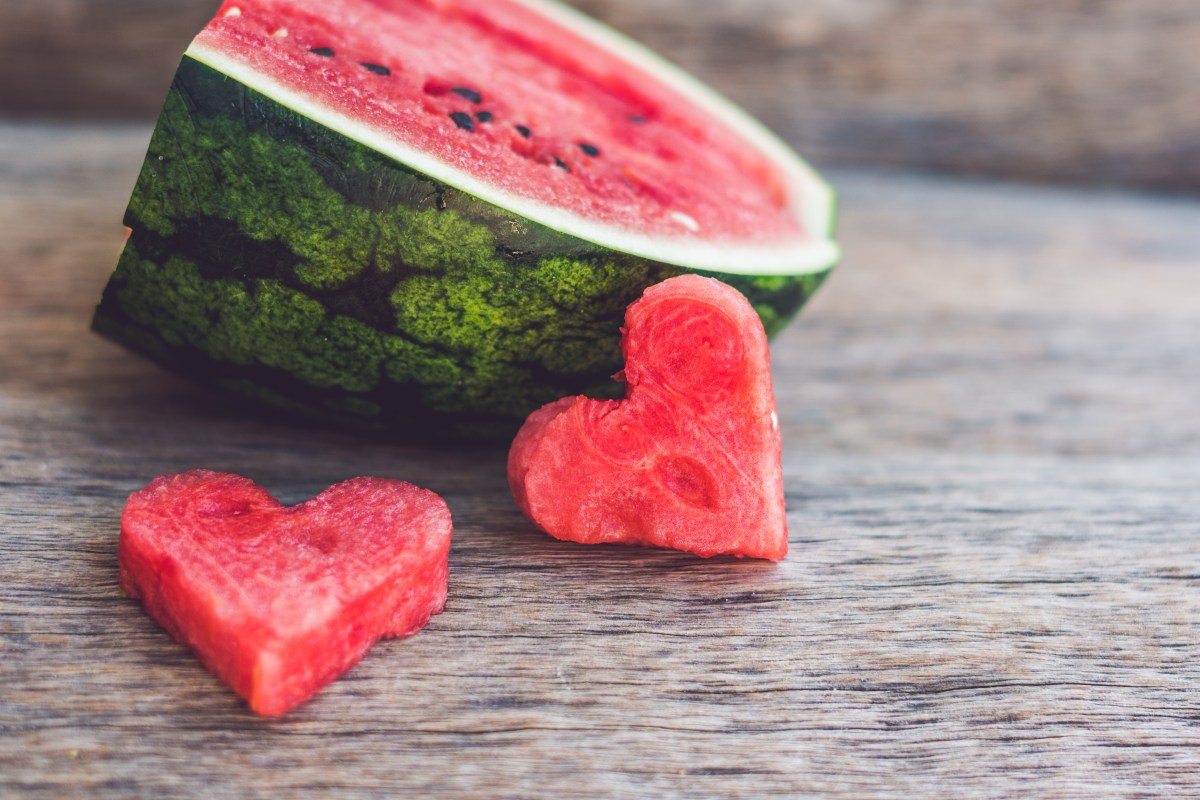 This image shows a watermelon which has had heart-shaped pieces of ripe watermelon flesh cut out of it and it is adorable. 
