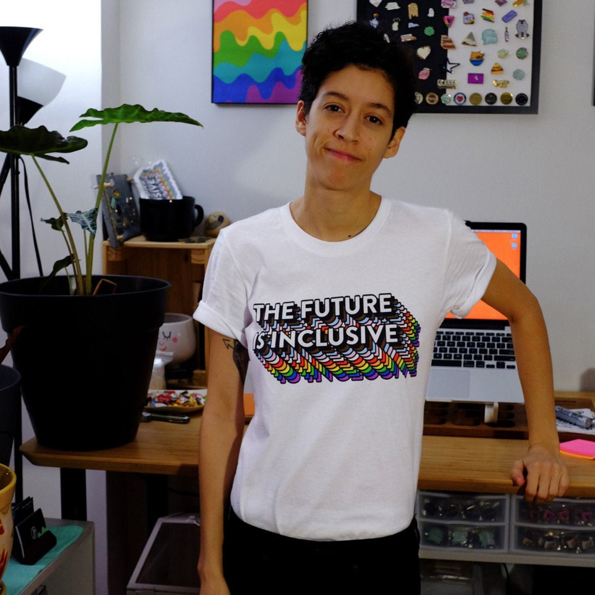 Model in an office wearing a white tee with the words THE FUTURE IS INCLUSIVE with rainbow shading