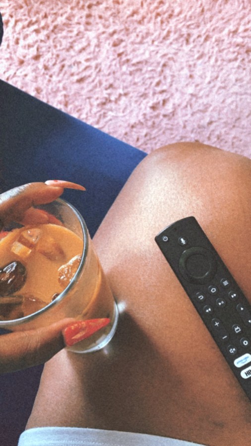 Shelli holding an iced coffee on her leg, a TV remote is also in view
