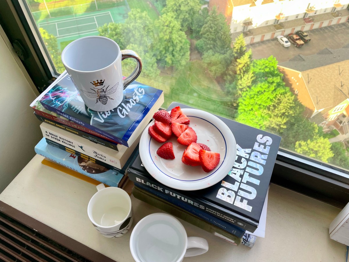 There are three mugs and a pile of cut up strawberries on top of books