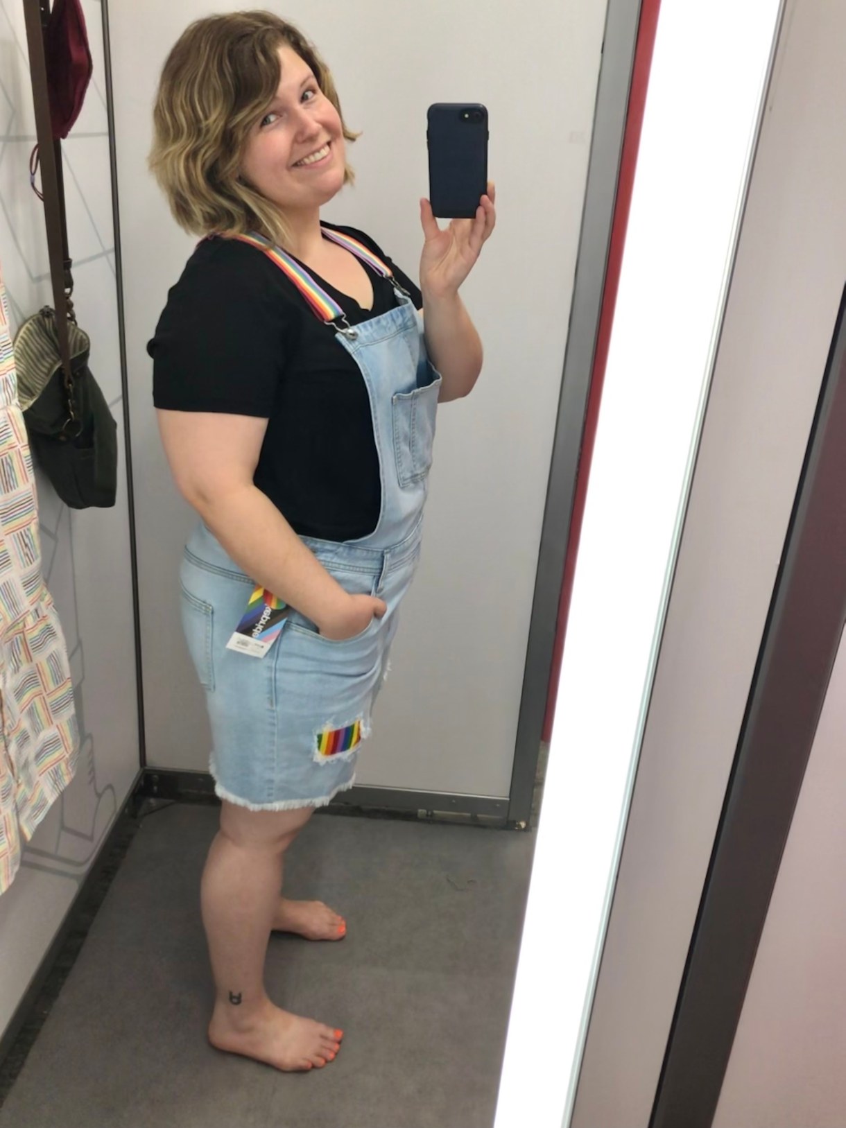 Caley posing in denim overalls in front of a mirror taking a selfie