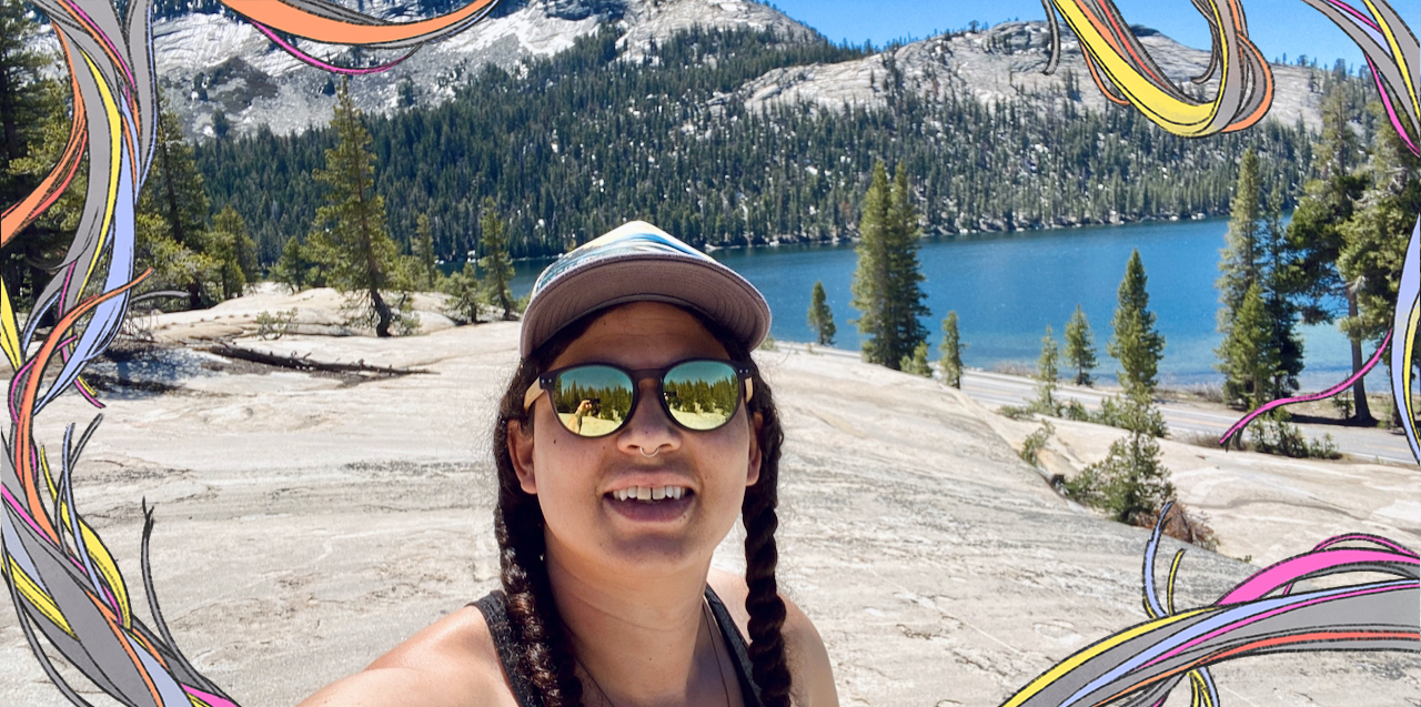 A feature image showing the author wearing sunglasses and two side braids with a baseball cap. She's standing in front of mountains and water at Yosemite.