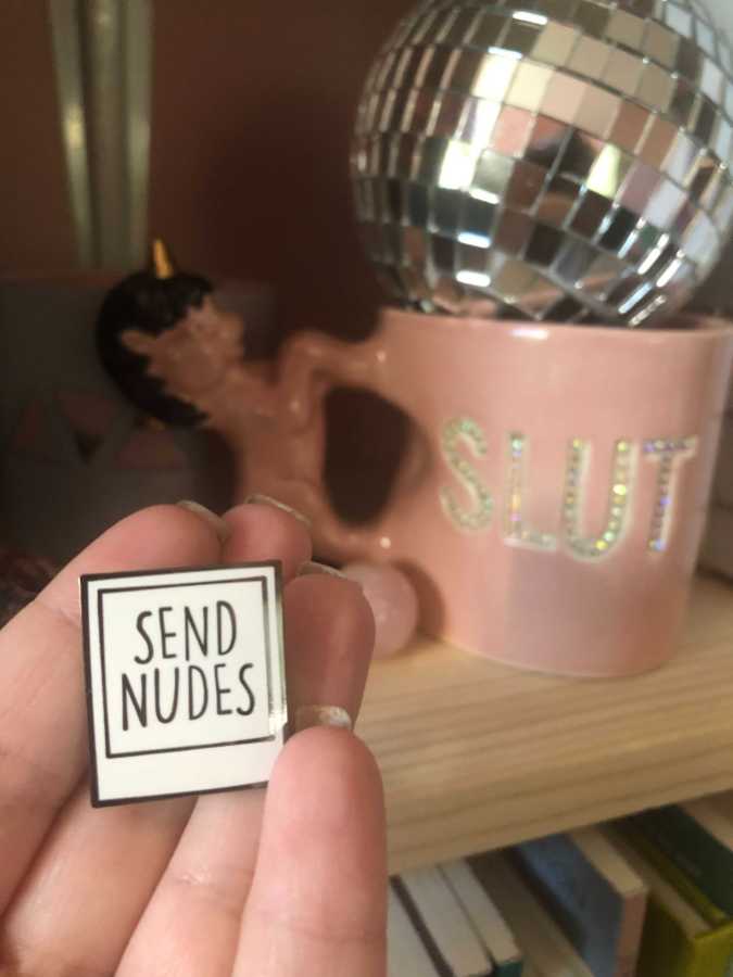 some items from vanessa's work area including a pin that says "send nudes" and a unicorn mug that says "slut"