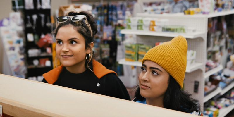 A still from the movie Plan B, with Lupe and Sunny standing at pharmacy looking for Plan B.