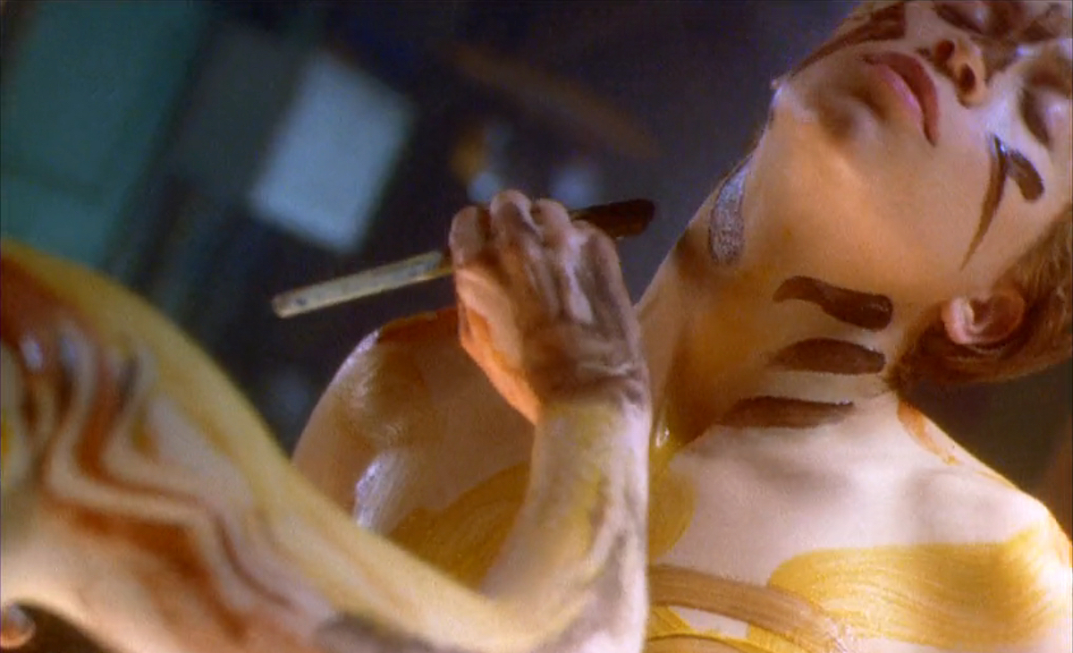 Lesbian sex scenes: A woman leans back in ecstasy as another woman paints lines on her with yellow and brown paints.