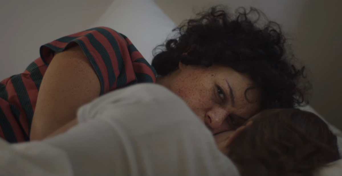 Alia Shawkat has her eyes open looking away as she lies in bed facing another woman.