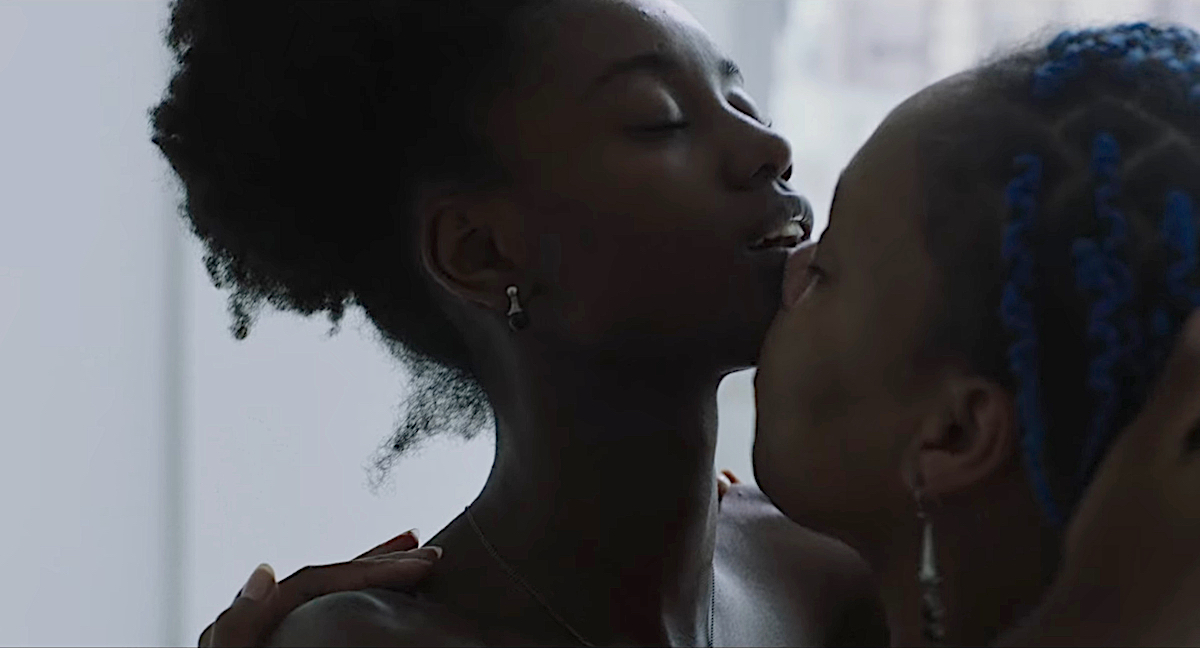 Lesbian sex scenes: A woman with blue braids kisses up another woman's neck to her chin.