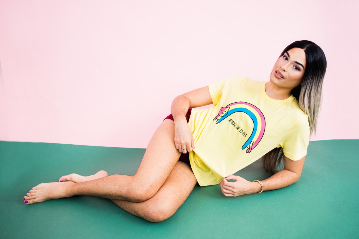 Model wearing a yellow t-shirt with a cat in an arc like the pansexual flag as a rainbow. the words "Amor Pa' Todes"